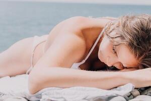 méconnaissable positif femme dans blanc bikini bain de soleil ou bronzage sur bord de mer plage pendant été. content touristique profiter Soleil bronzer mensonge sur plage chaise salon à luxe recours photo