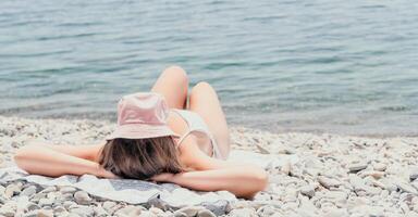 méconnaissable positif femme dans blanc bikini bain de soleil ou bronzage sur bord de mer plage pendant été. content touristique profiter Soleil bronzer mensonge sur plage chaise salon à luxe recours photo