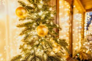 une Noël arbre avec or ornements et lumières. le arbre est décoré avec or des balles et est allumé en haut avec lumières. le arbre est mis dans une pièce avec une fenêtre photo