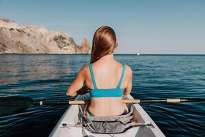 femme dans kayak retour voir. content Jeune femme avec longue cheveux flottant dans kayak sur calme mer. été vacances vacances et de bonne humeur femelle gens relaxant ayant amusement sur le bateau. photo