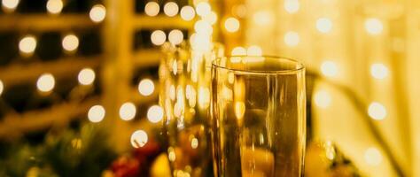 deux Champagne des lunettes rempli avec Champagne sont mis sur une table avec une fruit arrangement. le des lunettes sont entouré par lumières, création une de fête atmosphère. photo