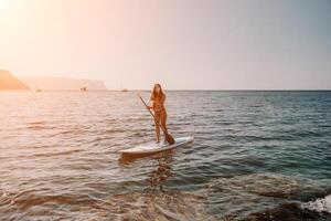 femme mer souper. proche en haut portrait de content Jeune caucasien femme avec longue cheveux à la recherche à caméra et souriant. mignonne femme portrait dans une bleu bikini posant sur souper planche dans le mer photo