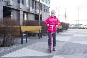 peu fille équitation une scooter dans le parc sur une ensoleillé printemps journée. actif loisir et Extérieur sport pour les enfants photo