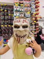 Podgorica, Monténégro - 14 août 2023. peu fille dans le boutique en essayant sur une effrayant zombi masque photo
