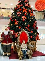 boudva, Monténégro - 25 décembre 2022. peu fille est assis sur un fauteuil près le Noël arbre dans le centre commercial photo