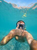 homme dans des lunettes de protection et palmes nage en dessous de l'eau avec le sien pouce en haut photo