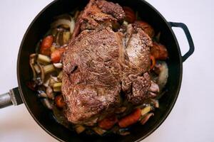 friture la poêle avec rouge rôti du boeuf avec des légumes des stands sur une blanc tableau. Haut vue photo