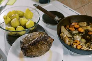 rôti du boeuf mensonges sur une assiette suivant à une la poêle avec cuit des légumes et une bol de entier cuit patates photo