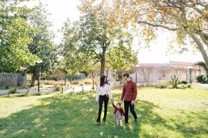 papa des promenades suivant à maman de premier plan une peu fille par le main dans le parc photo