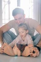 peu fille est assis avec sa papa sur le lit et examine leur nu pieds photo