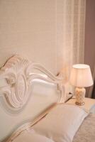 blanc double lit avec une sculpté haute retour dans le chambre suivant à une embrasé lampe sur le la table de nuit photo