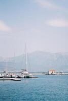 voile catamaran des stands à le jetée dans le mer contre le toile de fond de le montagnes. retour vue photo