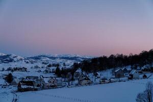 rose le coucher du soleil plus de une couvert de neige petit village dans une Montagne vallée à le bord de le forêt photo