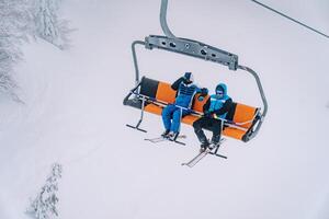 skieurs dans ski costume et des lunettes de protection balade sur une télésiège au dessus le neigeux des arbres photo