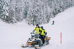 touristes dans Jaune ski costume balade une motoneige de une couvert de neige Montagne le long de le forêt photo