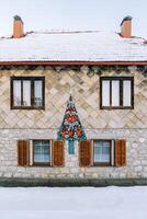 se sentait Noël arbre avec rouge arcs et guirlandes sur le façade de une à deux étages maison avec une couvert de neige toit photo