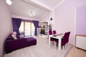 violet studio appartement avec une double canapé, une la télé sur le cabinet et une table avec chaises photo