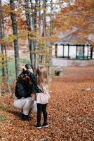 peu fille jette sec feuilles plus de sa mère squat dans un l'automne parc. retour vue photo