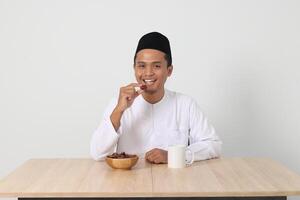 portrait de excité asiatique musulman homme en mangeant Kurma ou Date fruit pendant sahur et rupture rapide. culture et tradition sur Ramadan mois. isolé image sur blanc Contexte photo