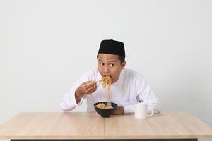 portrait de attrayant asiatique musulman homme en mangeant de bon goût instant nouilles avec baguettes servi sur bol. iftar et pré Aube repas concept. isolé image sur blanc Contexte photo