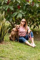 portrait de une femme portant des lunettes de soleil embrassement sa animal de compagnie. photo