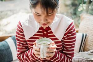 proche en haut de une contenu Jeune femme en portant une tasse de matcha thé, profiter le chaleur et arôme dans une confortable café paramètre. photo