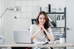 souriant femme d'affaires est assis en toute confiance à sa rangé bureau dans une moderne, bien éclairé Bureau environnement. photo