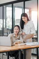 deux souriant femelle collègues en collaboration travail sur une projet avec une portable et café dans une brillant Bureau espace. photo