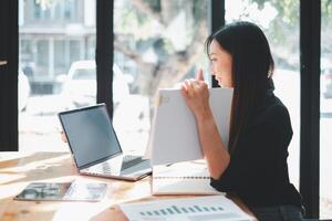 concentré femme révision les documents avec portable ouvert dans une ensoleillé espace de travail, symbolisant diligence et productivité dans affaires planification. photo