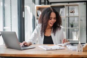 femme d'affaires profondément absorbé dans croquer Nombres et gérant finances sur sa calculatrice, avec une portable et les documents sur sa bureau. photo