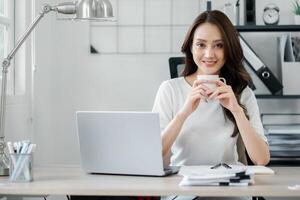 souriant Jeune professionnel femme prise une café Pause à sa rangé et élégant Accueil Bureau bureau, incorporant une détendu travail atmosphère. photo