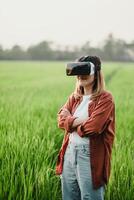 sur de soi Jeune femme des stands avec bras franchi dans une luxuriant vert champ, portant une vr casque, prêt à explorer virtuel paysages. photo