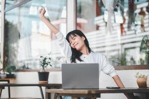 une femme s'étire avec une content sourire pendant une Pause de travail, entouré par le apaisant ambiance de sa brillant, orné de plantes Accueil bureau. photo