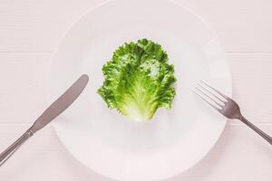 feuille salade sur blanc assiette avec fourchette et couteau, Haut vue sur en bois table photo