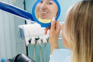 le fille sourit et regards dans le miroir dans dentisterie photo