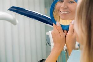 le fille sourit et regards dans le miroir dans dentisterie photo