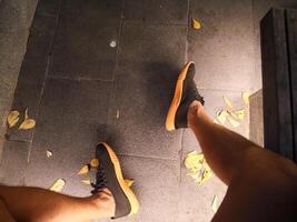 jambes et pieds de une homme portant baskets sur une ciment sol jonché avec fleur pétales à nuit le lumières éclat sur photo