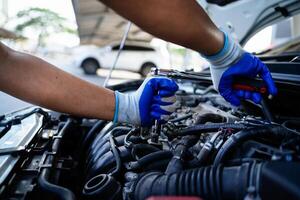 une mécanicien est travail sur une voiture moteur, portant bleu gants. le voiture est garé suivant à une blanc voiture photo