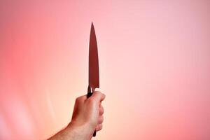 une homme détient une couteau dans le sien main. isolé sur rouge Contexte photo