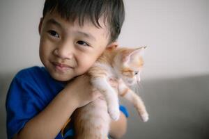 une Jeune garçon est en portant une chaton dans le sien bras photo