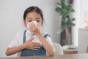 enfant asiatique fille malade avec des éternuements sur le nez et une toux froide sur du papier de soie parce que faible ou virus et bactéries du temps de la poussière photo