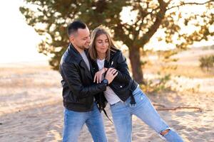 content et mignonne adorable adulte couple de millénaire les hipsters, homme avec femme petite amie marche, avoir amusement jouer, rire sourire et sauter sur le coucher du soleil à désert photo