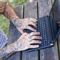 mains de une tatoué homme travail avec ordinateur Extérieur photo
