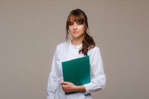 portrait de une femelle médical ouvrier dans une gris Contexte avec une médical rapport.fille médecin avec une bloc-notes photo