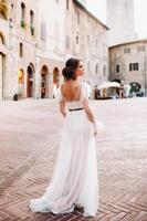 une la mariée dans une blanc robe dans le vieux ville de san gimignano.a fille des promenades autour le ville dans italie.toscane. photo