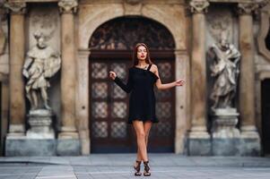 élégant Jeune fille dans une noir robe dans Urbain style sur le rue de le ville de Brno. tchèque photo