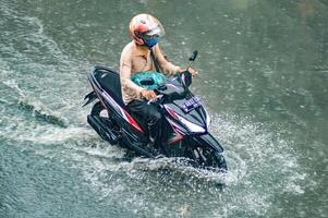 une motocycliste qui a conduit par inonder des eaux pendant lourd pluie dans une Résidentiel zone, Indonésie, 8 décembre 2023. photo