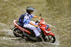 une haute école étudiant qui monte une moto qui disques par inonder des eaux pendant lourd pluie dans une Résidentiel zone, Indonésie, 8 décembre 2023. photo