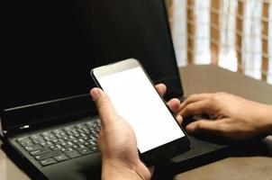 main tenant l'image de la maquette du téléphone à écran blanc ordinateur portable pour le texte publicitaire dans le bureau du lieu de travail au bureau. photo