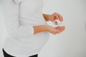 proche en haut sur Enceinte ventre avec médecine..femme attendant une bébé habillé dans blanc en portant pilules. prise drogues ou vitamines pendant grossesse concept. photo